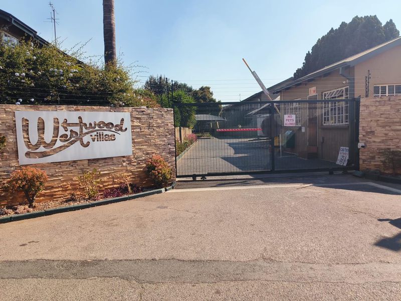 The entrance to Westwood Villas featuring a secure electric gate, stone-clad boundary wall, and electric fencing for enhanced property security.