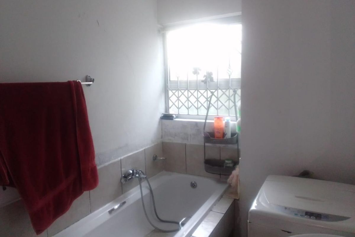 A functional bathroom featuring a bathtub with a handheld shower mixer, tiled splashback, and a window with security bars.