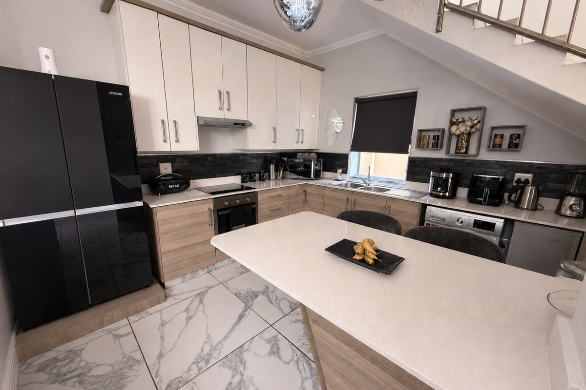 Modern kitchen featuring two-tone cabinetry, stone countertops, marble-look floor tiles, and an integrated breakfast island, situated beneath a staircase.