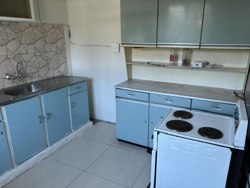 A dated kitchen featuring blue cabinetry, a stainless steel sink, tiled splashback, and a freestanding electric stove with tiled flooring.