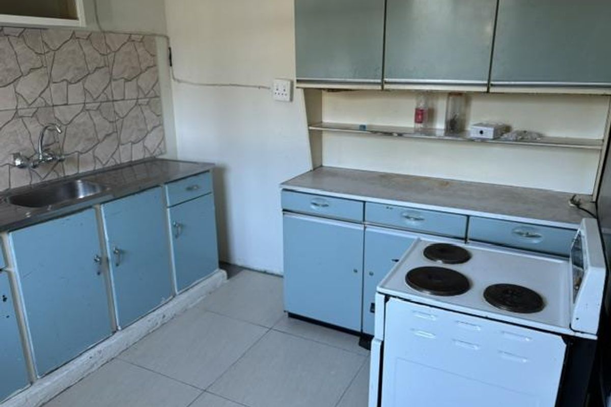 A dated kitchen featuring blue cabinetry, a stainless steel sink, tiled splashback, and a freestanding electric stove with tiled flooring.