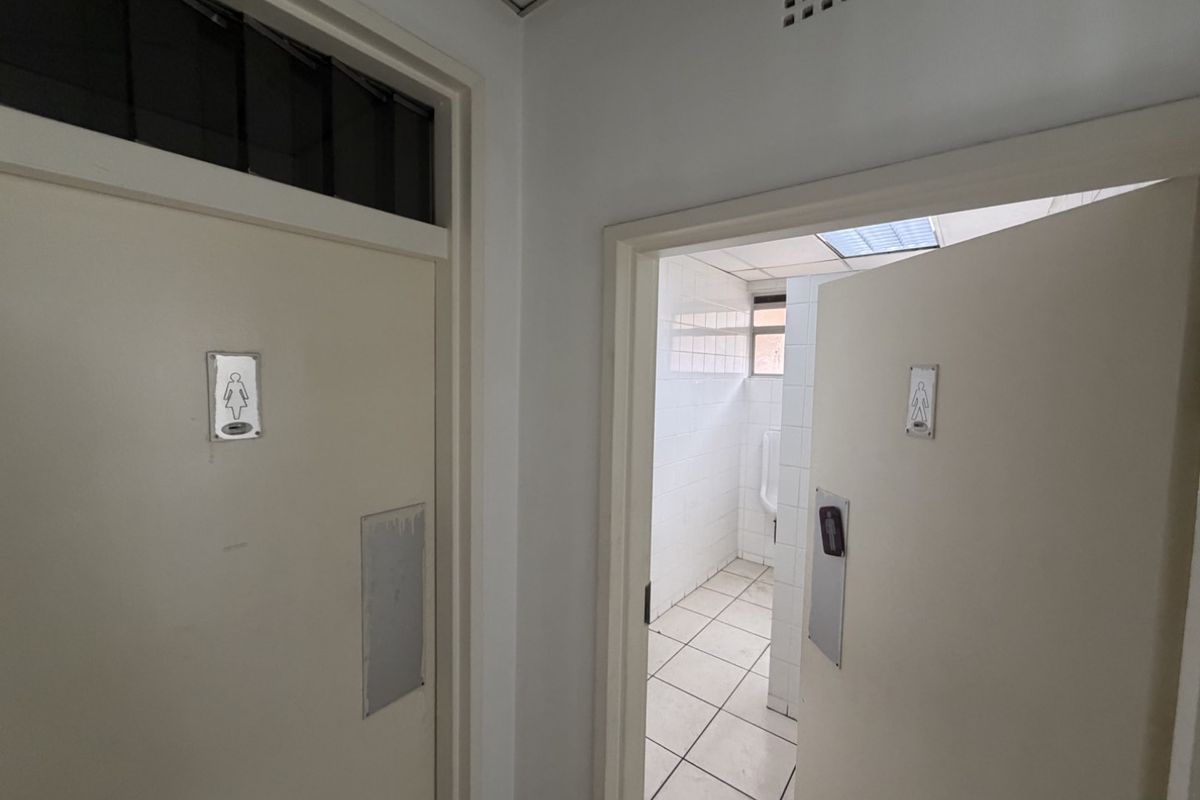A functional industrial restroom facility featuring separate gender-designated entrances, tiled surfaces, and a urinal area.