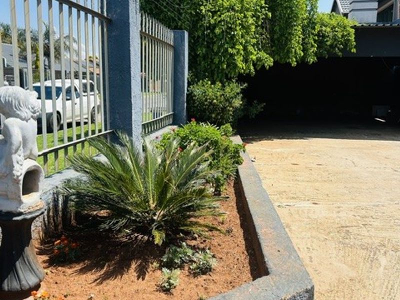 Front exterior view featuring a concrete driveway, raised garden bed, and metal perimeter fencing with integrated security wiring.