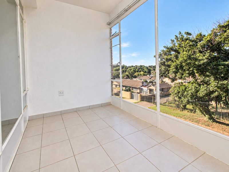 A bright, enclosed balcony featuring tiled flooring and expansive windows offering pleasant neighborhood views, perfect for a sunroom or relaxation area.