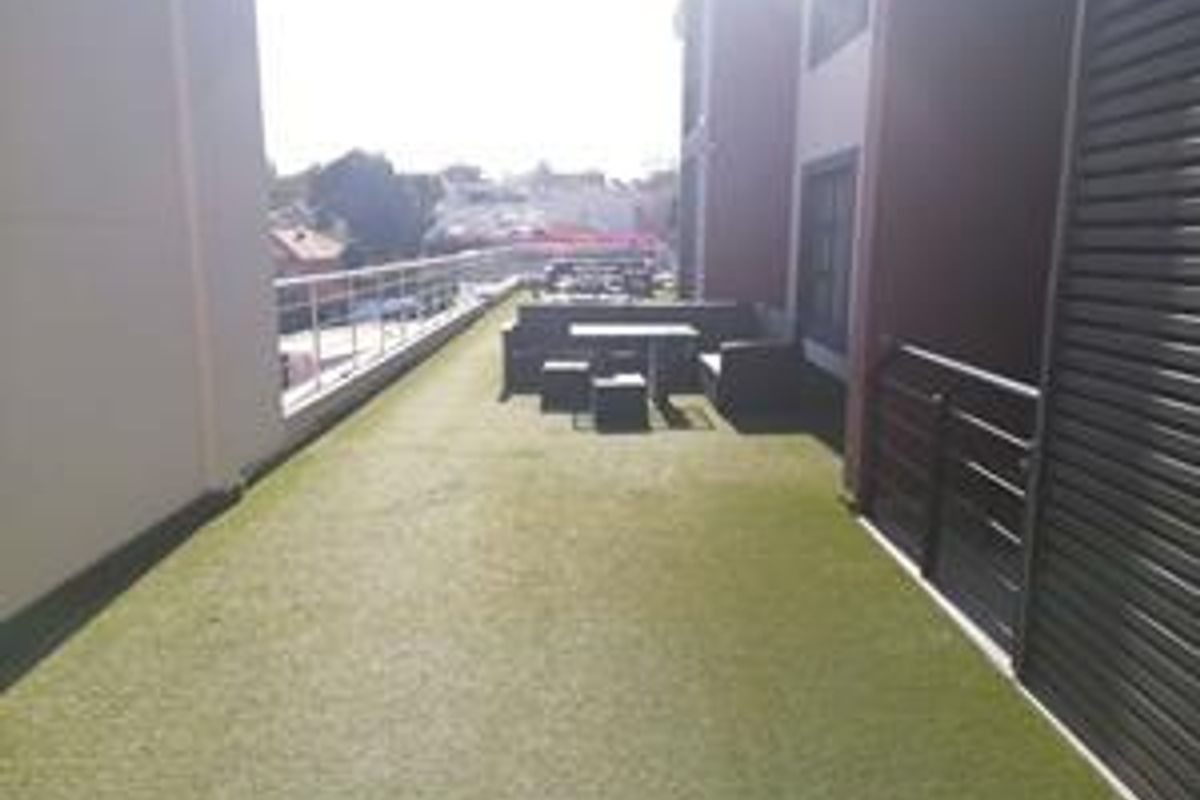 A spacious outdoor balcony featuring artificial turf flooring, a metal balustrade, and a slatted privacy screen, offering an open-air seating area.