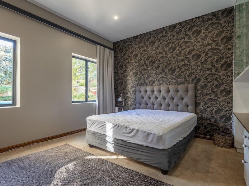 A well-maintained bedroom featuring a feature wallpaper wall, built-in cabinetry, and large windows providing natural light.
