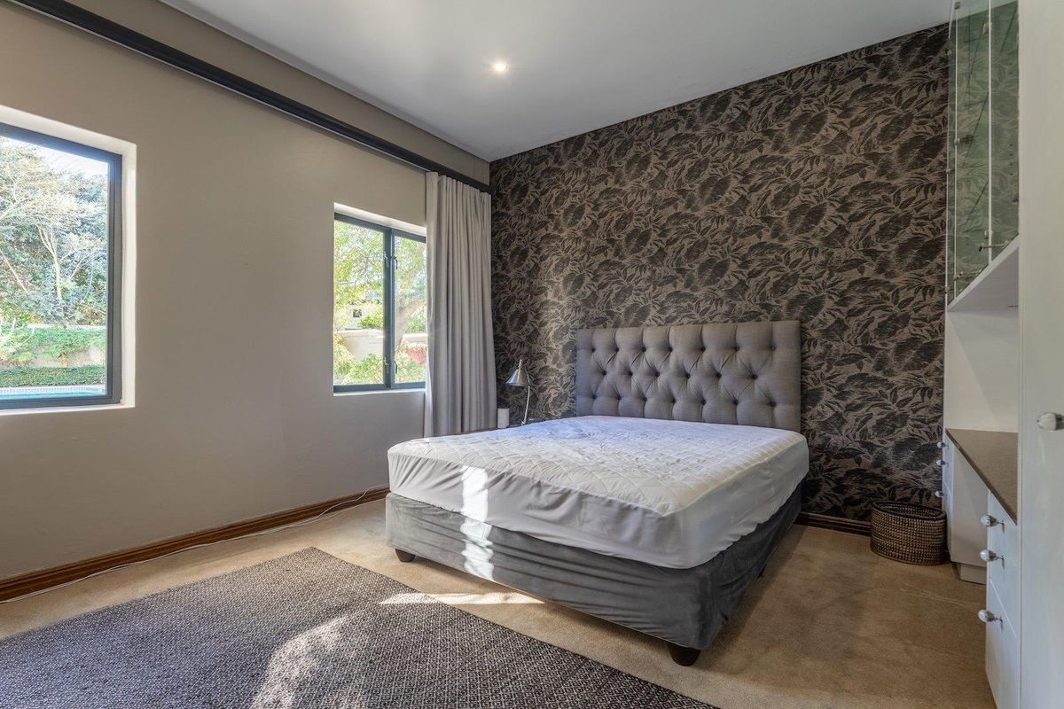 A well-maintained bedroom featuring a feature wallpaper wall, built-in cabinetry, and large windows providing natural light.