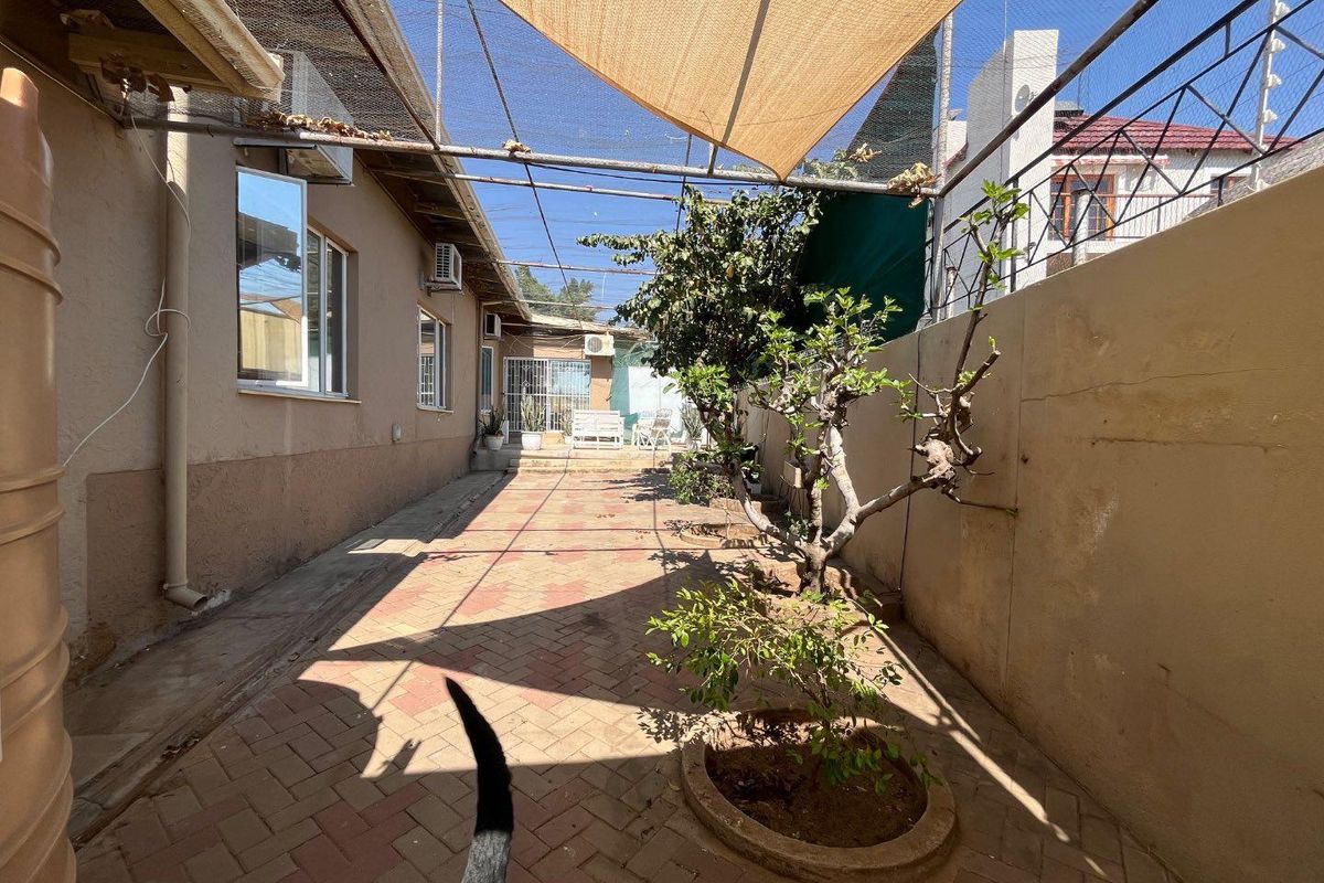 A paved rear courtyard featuring a shade sail, perimeter wall, and water tank, providing a functional outdoor space for relaxation.