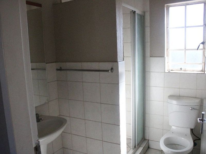 A functional bathroom featuring a pedestal basin, toilet, and a separate shower enclosure with tiled walls and a window for natural light.