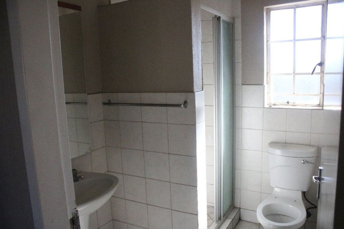A functional bathroom featuring a pedestal basin, toilet, and a separate shower enclosure with tiled walls and a window for natural light.