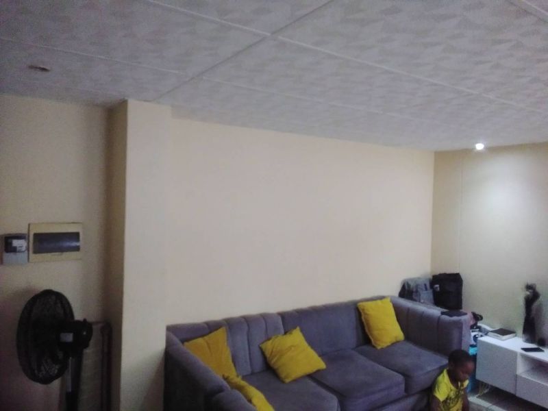 A living room area featuring a neutral wall finish, recessed ceiling lighting, and a visible electrical distribution board.