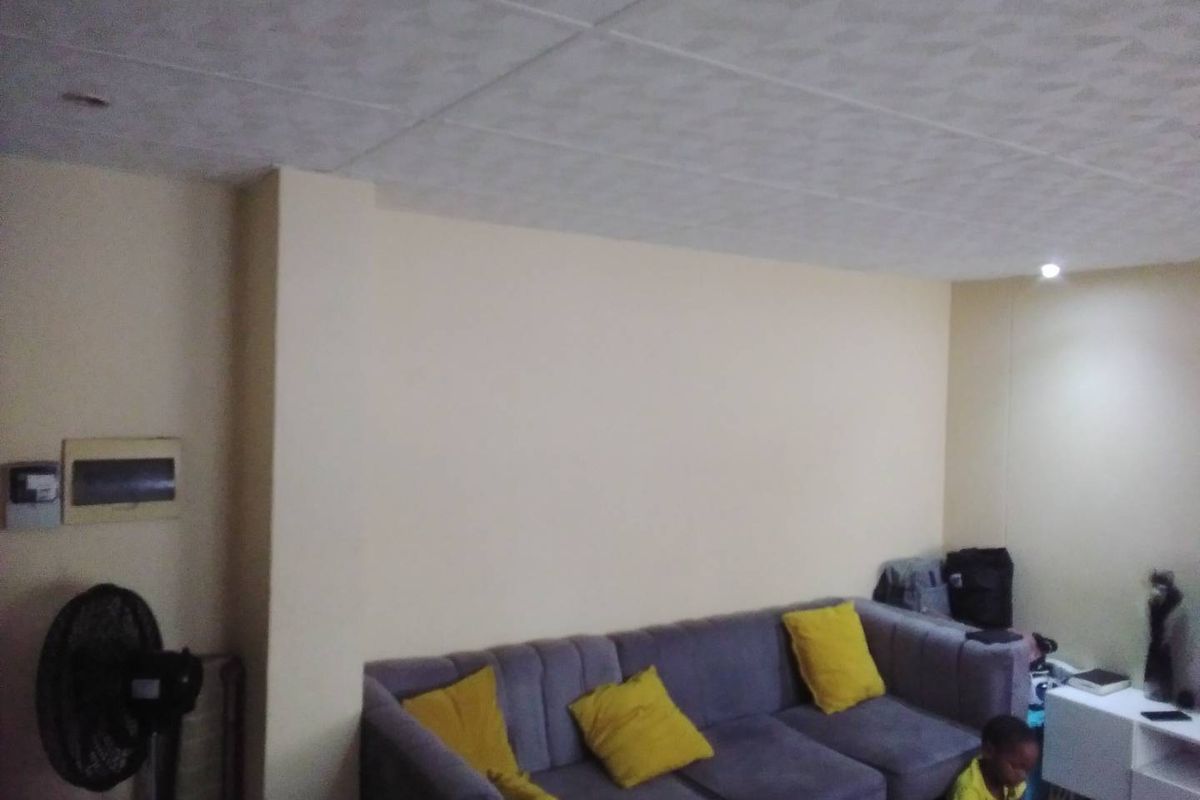 A living room area featuring a neutral wall finish, recessed ceiling lighting, and a visible electrical distribution board.