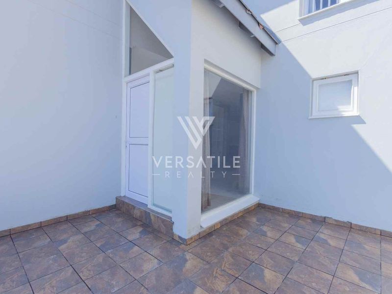 A clean, tiled outdoor patio area featuring a glass door entrance and a fixed window, providing a bright and functional transition space.