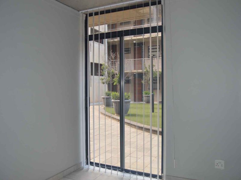 An empty living area featuring tiled flooring and a large sliding glass door with vertical blinds, providing access to an outdoor courtyard.