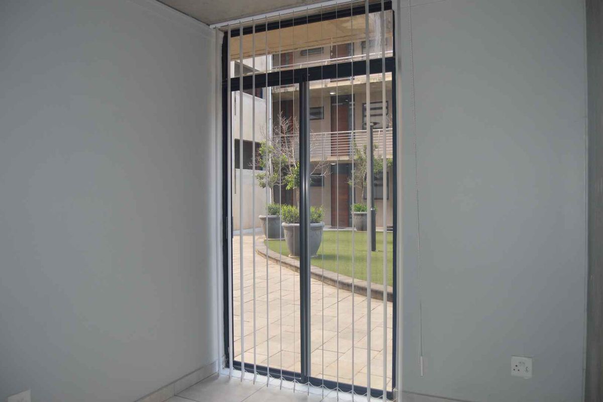 An empty living area featuring tiled flooring and a large sliding glass door with vertical blinds, providing access to an outdoor courtyard.