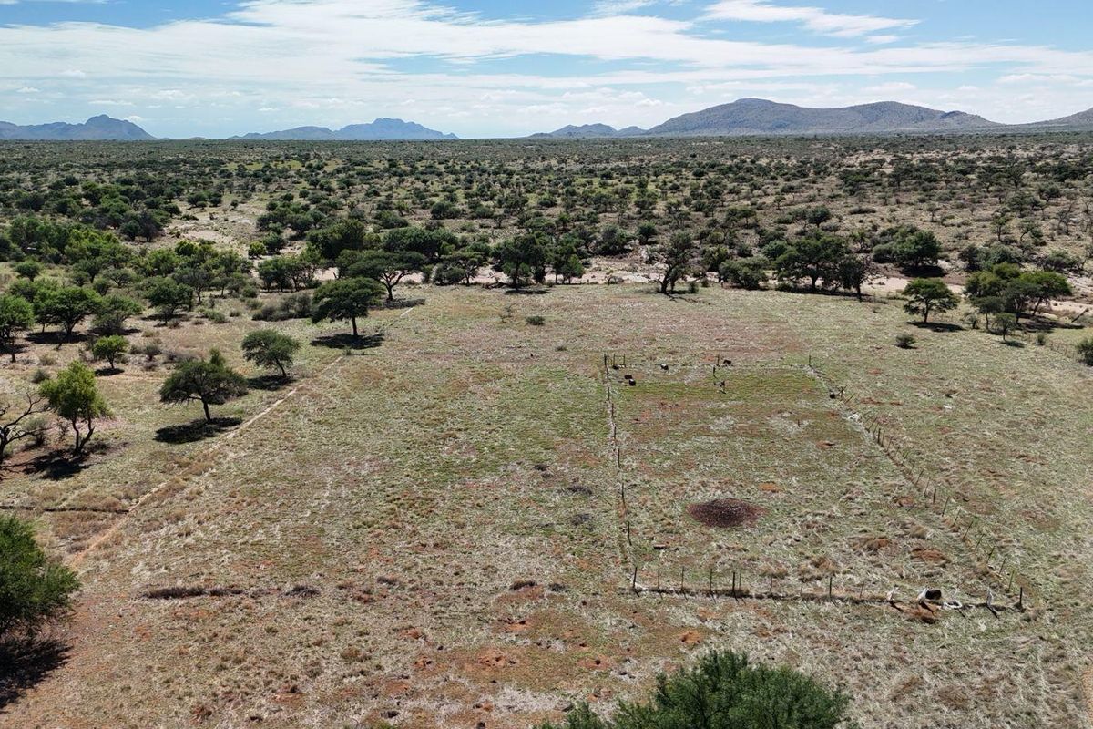 An aerial view of a large, open farm landscape featuring natural vegetation and sections of wire fencing.