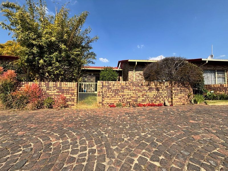 Front view of a townhouse featuring a cobblestone driveway, brick boundary wall, and secure gated entrance.