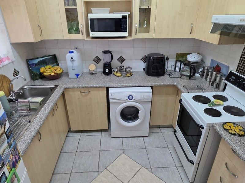 A functional kitchen featuring light wood-finish cabinetry, granite-look countertops, a tiled backsplash, and integrated appliances including a microwave and extractor fan.