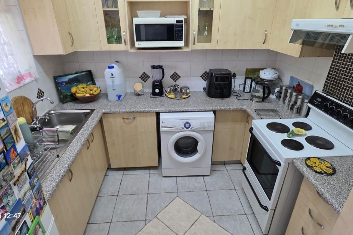 A functional kitchen featuring light wood-finish cabinetry, granite-look countertops, a tiled backsplash, and integrated appliances including a microwave and extractor fan.