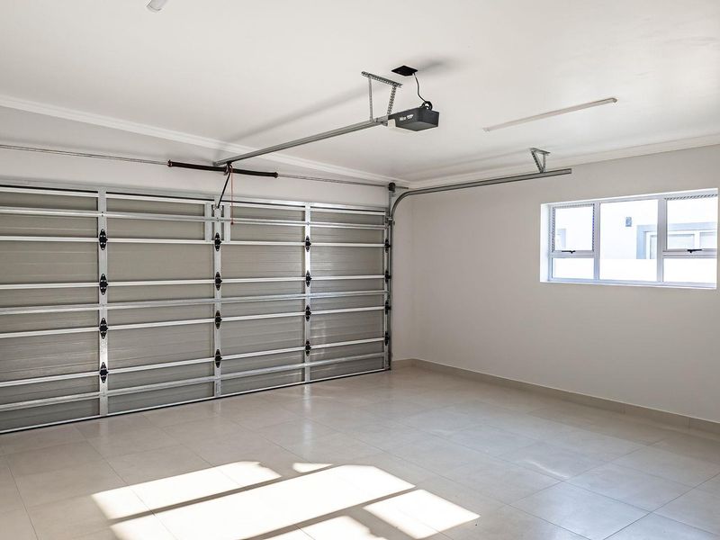 A clean, spacious, and well-maintained double garage featuring tiled flooring, a sectional door with an automatic opener, and a window for natural light.