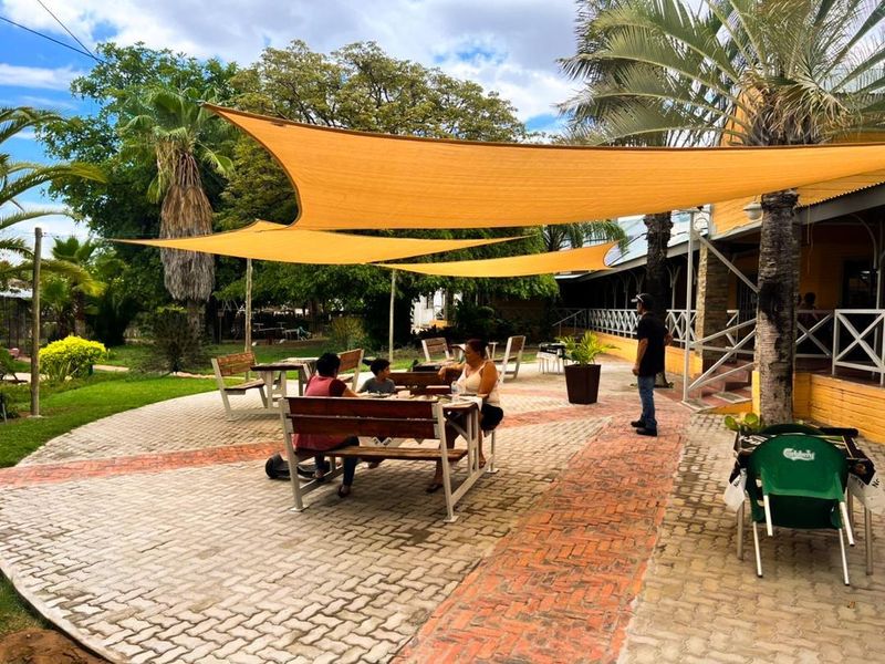 An outdoor patio area featuring paved flooring, overhead shade sails, and access to a landscaped garden space.