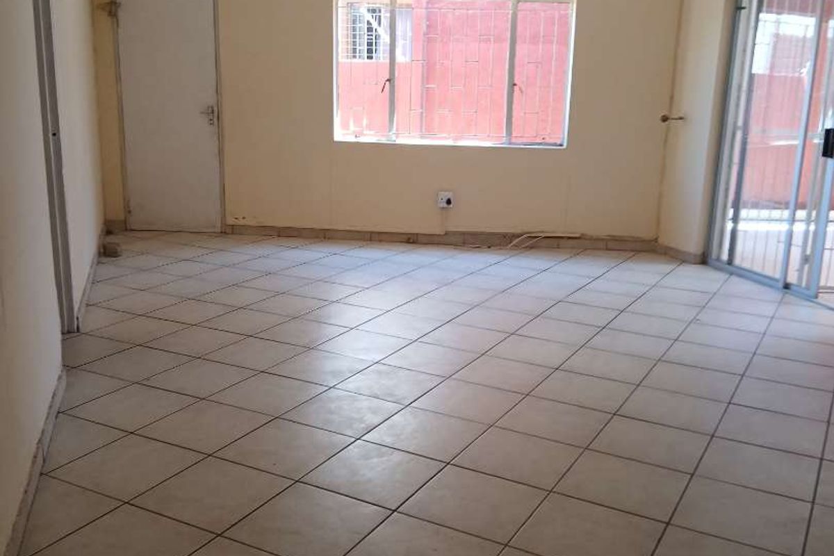 An empty living room featuring tiled flooring, a wall-mounted air conditioning unit, and sliding glass doors leading to an outdoor area.