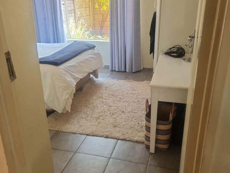 A bedroom featuring tiled flooring and a large window allowing natural light, providing a functional space with direct access to the garden area.