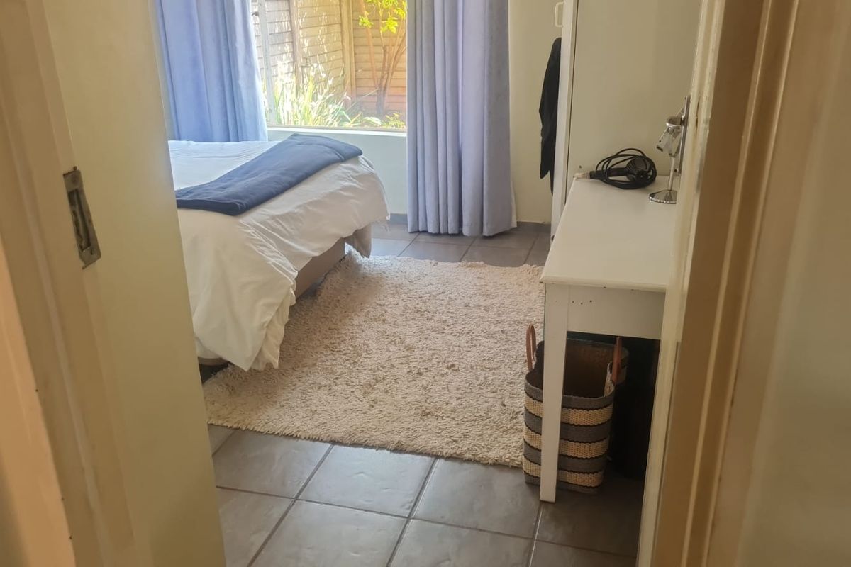 A bedroom featuring tiled flooring and a large window allowing natural light, providing a functional space with direct access to the garden area.