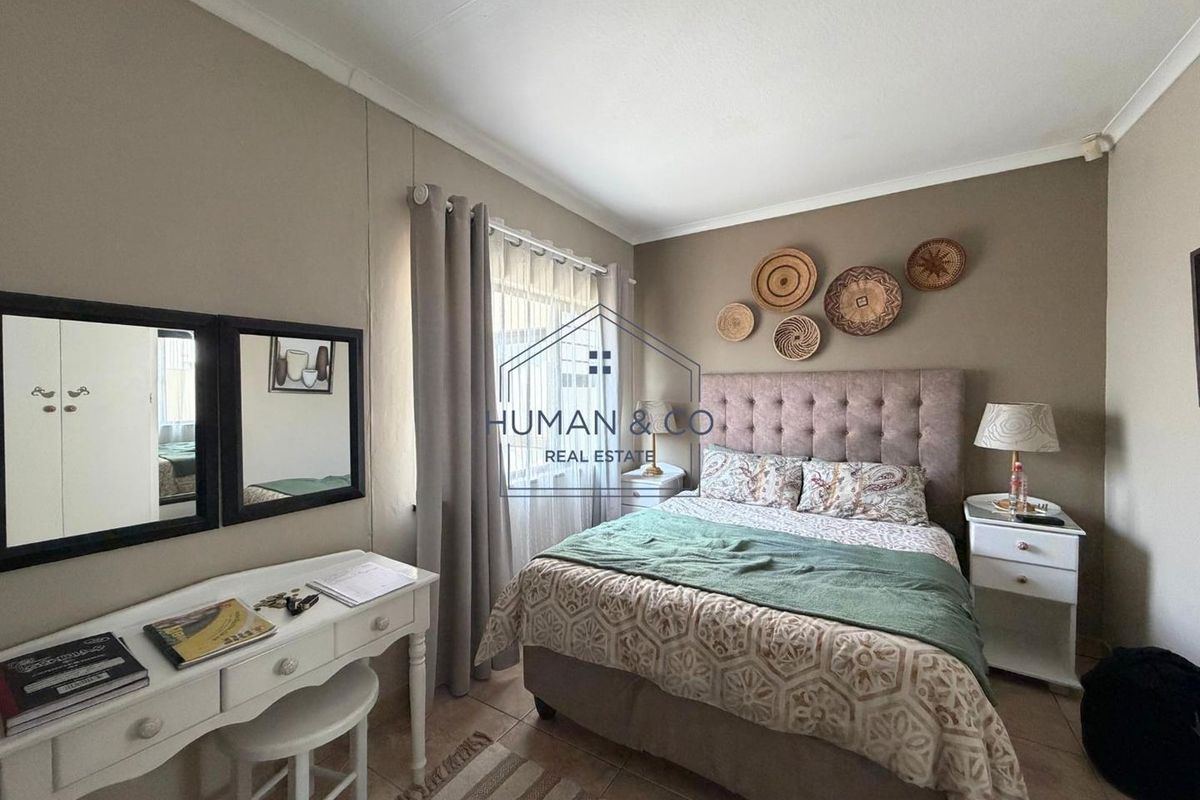 A well-maintained bedroom featuring neutral wall tones, tiled flooring, and large windows with curtain rails.