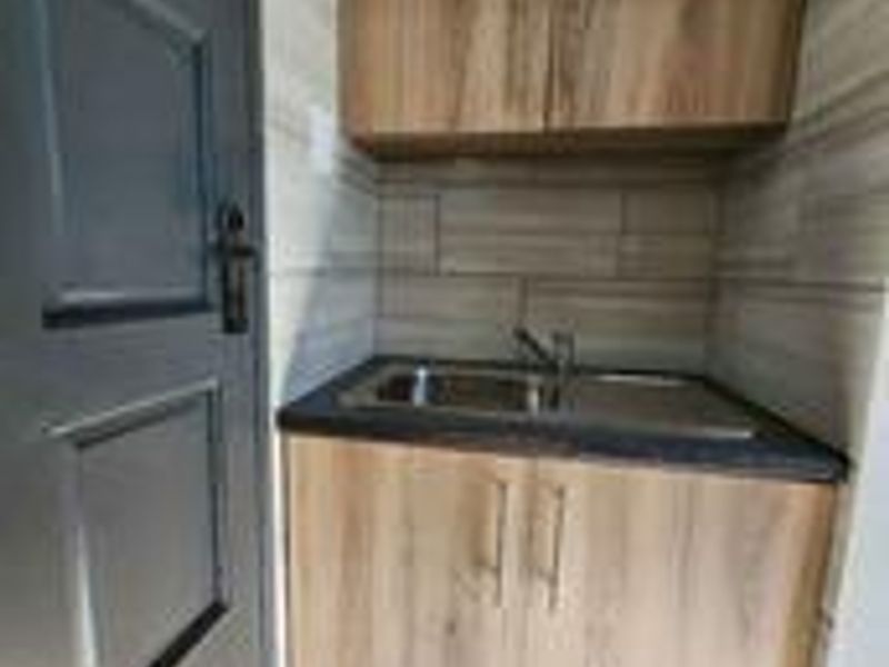 A compact laundry area featuring modern wood-look cabinetry, a stainless steel sink with mixer tap, and neutral tiled splashback.