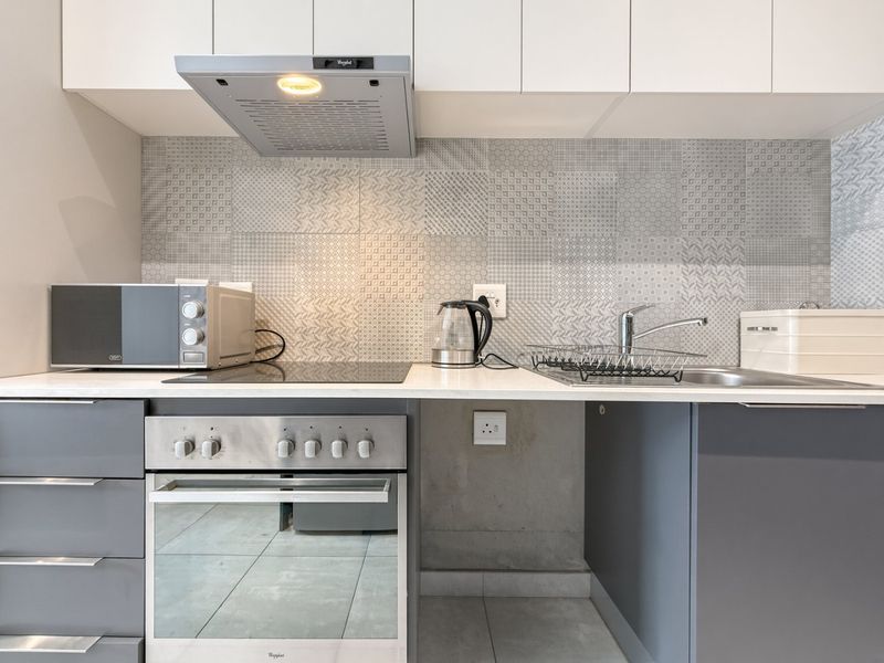 Modern kitchen featuring a built-in oven, electric hob, extractor fan, stainless steel sink, and stylish patterned tiled backsplash with ample cabinetry.