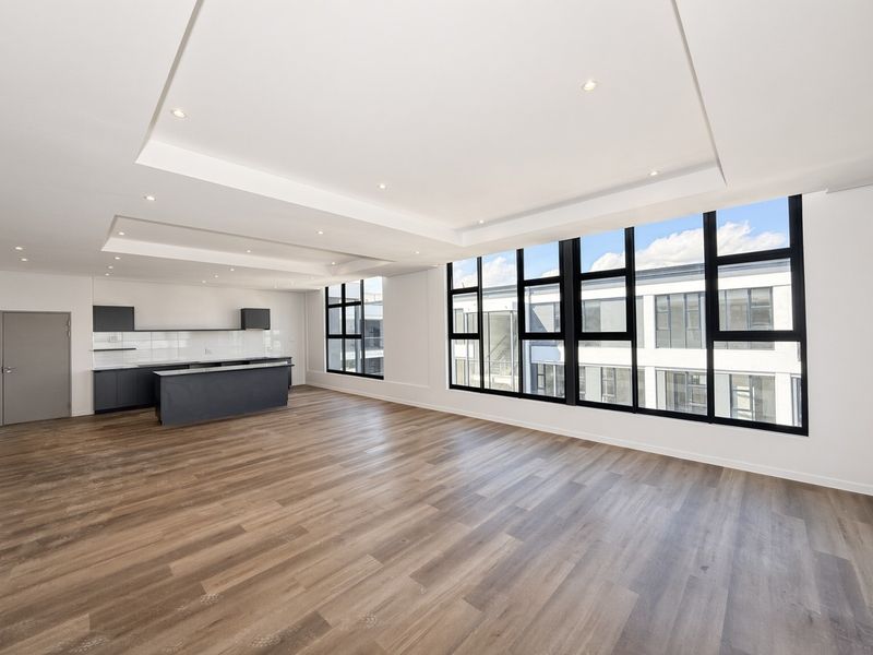 Spacious open-plan living area featuring modern laminate flooring, recessed ceiling lighting, and a sleek kitchen with dark cabinetry and a central island.