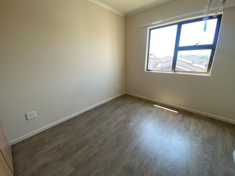 A clean, empty bedroom featuring modern laminate flooring, neutral walls, and an aluminium-framed window with natural light.