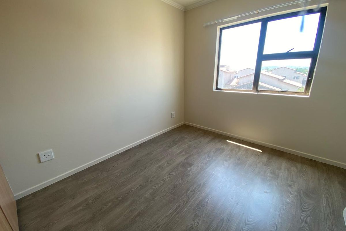 A clean, empty bedroom featuring modern laminate flooring, neutral walls, and an aluminium-framed window with natural light.