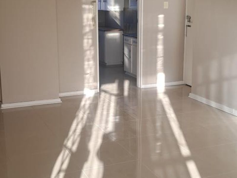 A bright, empty living area featuring neutral tiled flooring and a view through to the kitchen area.