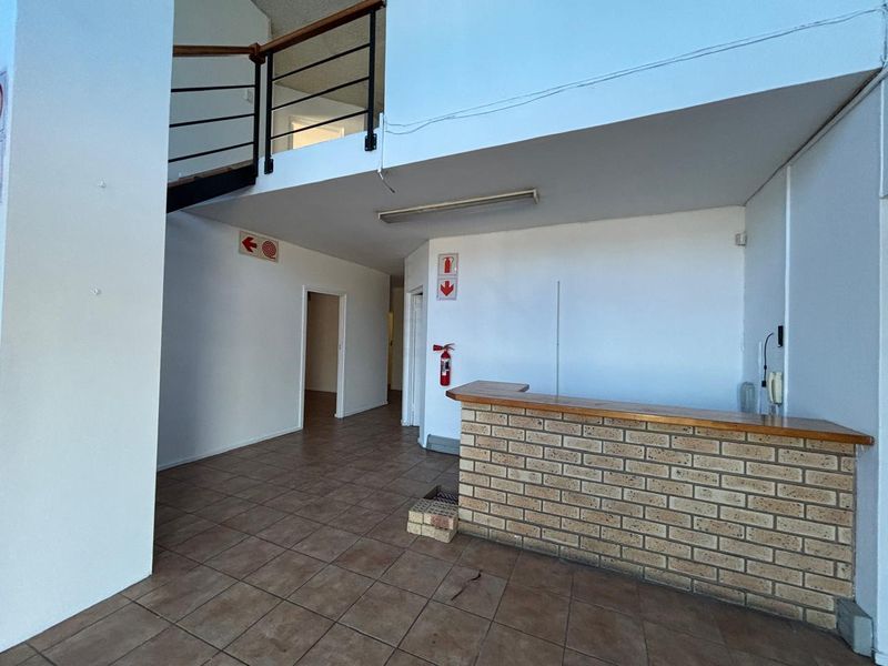 Spacious industrial entry area featuring a brick reception counter, tiled flooring, and an open staircase leading to an upper level.