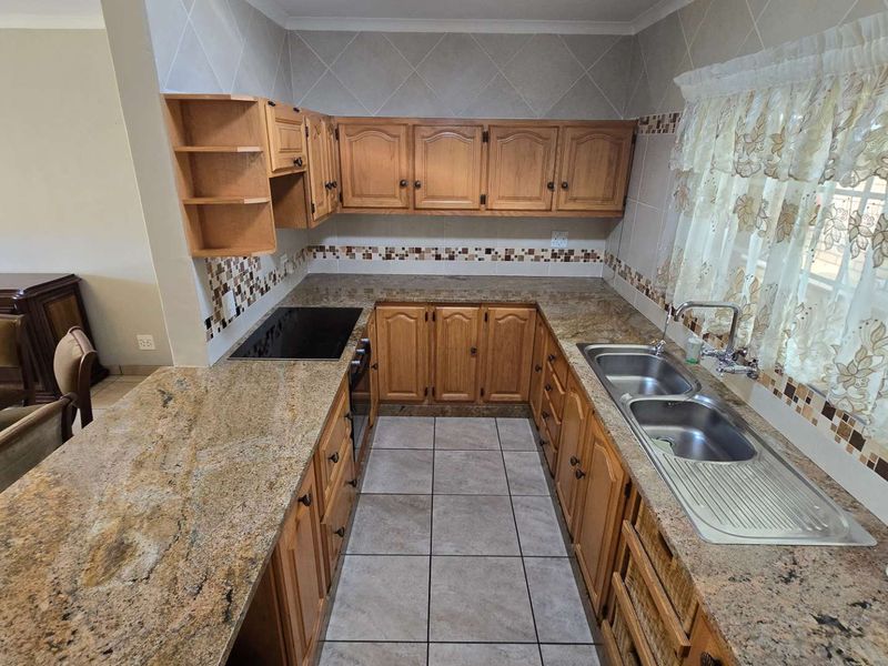 A functional kitchen featuring granite countertops, double stainless steel sink, built-in wooden cabinetry, and tiled flooring with a decorative backsplash.