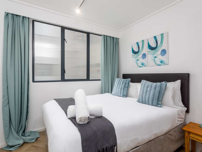 A well-maintained bedroom featuring timber flooring, a dark metal-framed window with fluted glass, and a recessed ceiling spotlight.