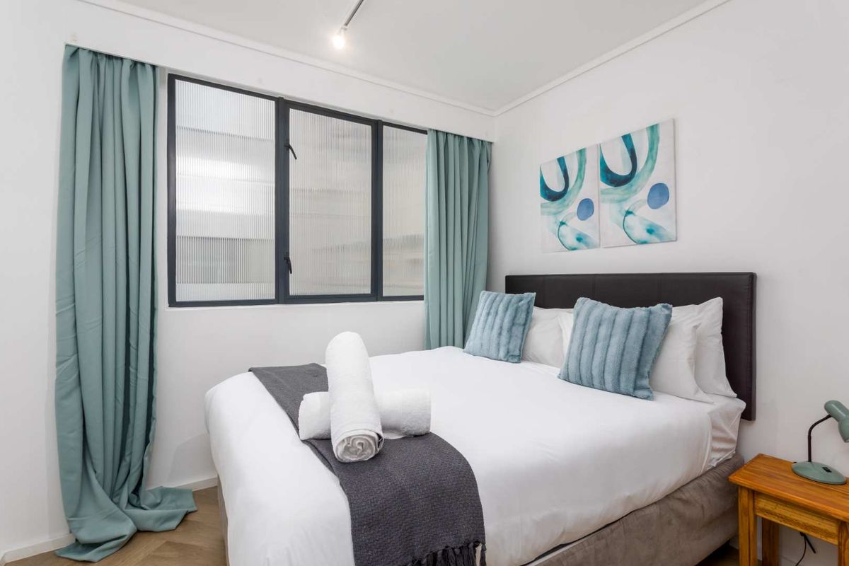 A well-maintained bedroom featuring timber flooring, a dark metal-framed window with fluted glass, and a recessed ceiling spotlight.