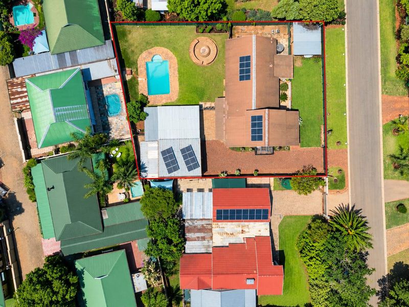 Aerial view of the property showcasing the residential layout, including a swimming pool, solar panel installation, paved driveway, and established garden areas.