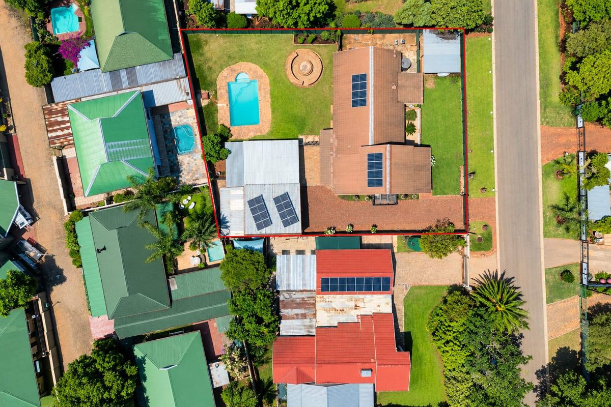 Aerial view of the property showcasing the residential layout, including a swimming pool, solar panel installation, paved driveway, and established garden areas.