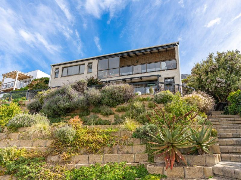 Rear elevation of a multi-level home featuring a terraced garden with stone retaining walls, a staircase, and an upper-level balcony with glass balustrades.