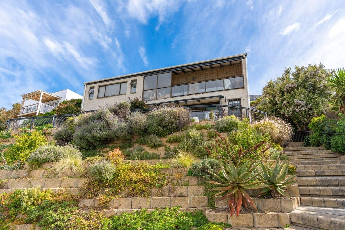 Rear elevation of a multi-level home featuring a terraced garden with stone retaining walls, a staircase, and an upper-level balcony with glass balustrades.
