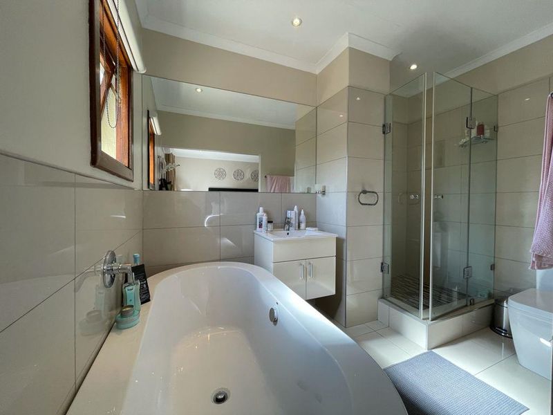 Modern bathroom featuring a freestanding bathtub, glass-enclosed shower, wall-mounted vanity, and large mirror with neutral tiling throughout.