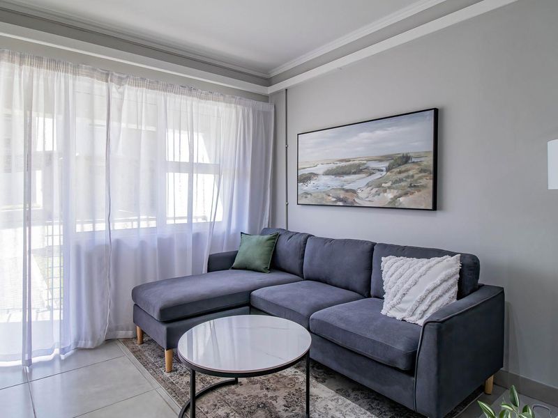 A well-maintained living room featuring neutral grey walls, crown molding, tiled flooring, and a large sliding glass door providing natural light.