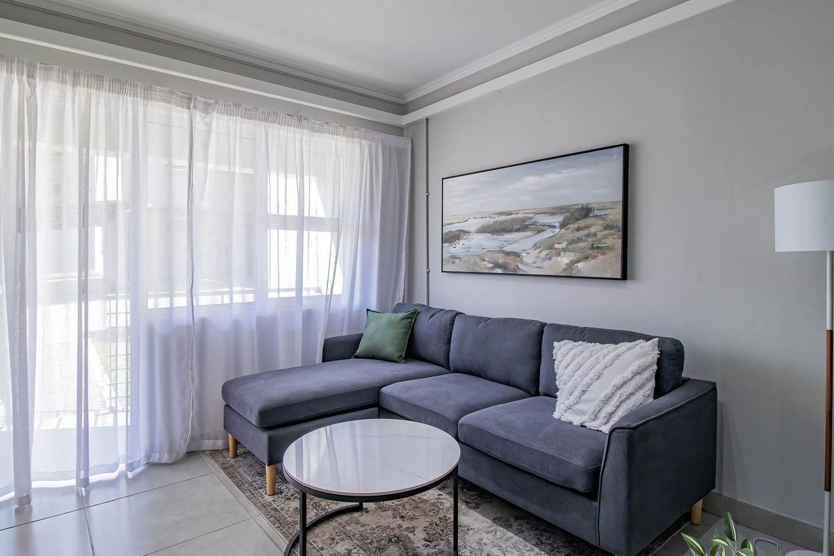 A well-maintained living room featuring neutral grey walls, crown molding, tiled flooring, and a large sliding glass door providing natural light.