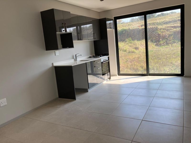 Modern open-plan kitchen featuring sleek dark cabinetry, stone countertops, and integrated appliances, with direct access to an outdoor area through large sliding glass doors.