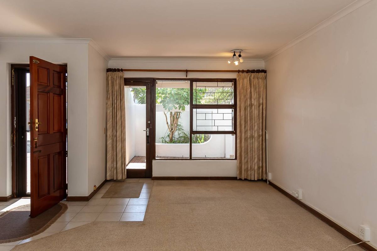 A bright living area featuring a solid timber entrance door, large windows with security bars, and direct access to a private outdoor courtyard.