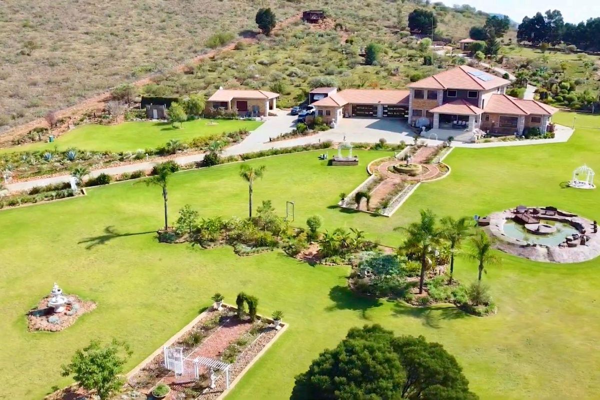 Aerial view of a large residential estate featuring extensive landscaped gardens, a water feature, paved driveway, and a multi-car garage structure.