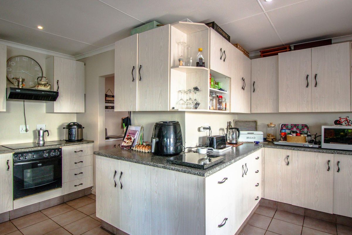 A functional kitchen featuring light wood-grain cabinetry, granite countertops, a built-in oven, and a ceramic hob with an extractor fan.